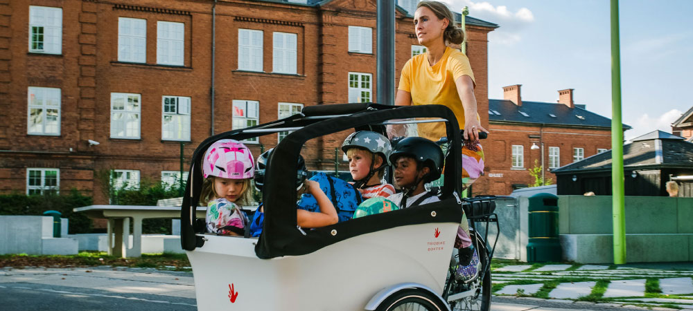 Eine Frau fährt mit dem Cargobike von Triobike und 4 Kindern über die Straße
