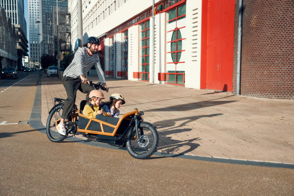 Mann fährt mit zwei Kindern mit einem Cargobike von Riese & Müller